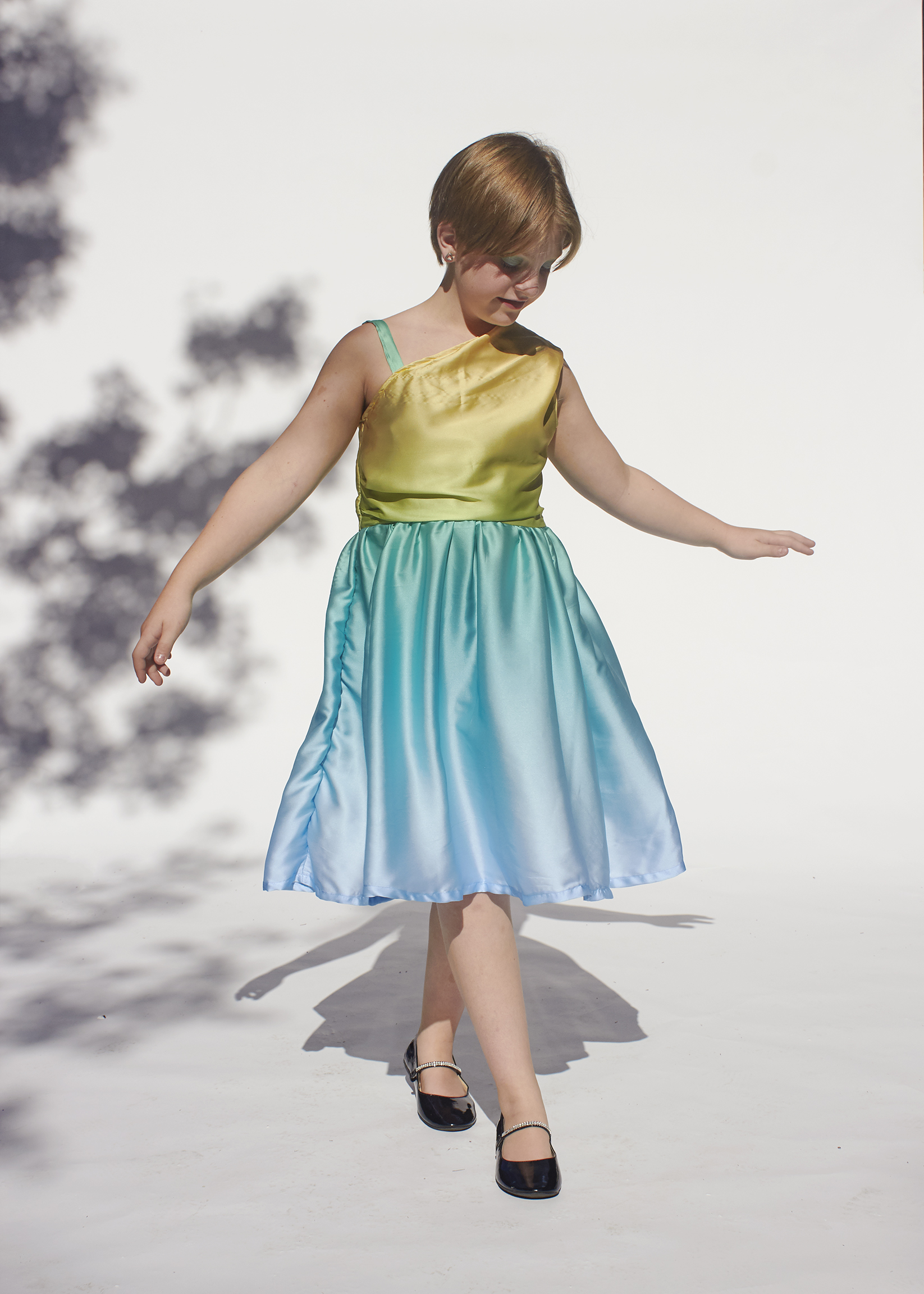 There is a girl spinning in her handmade on shoulder yellow and aqua dress