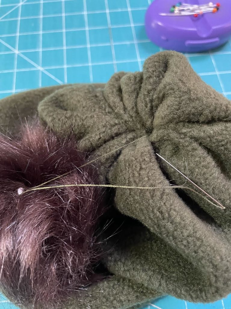 adding faux fur pom pom to top of hat