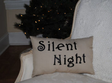 A tan pillow with iron on writing that says Silent Night