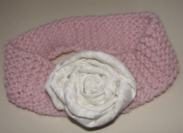 knitting using pink yarn to make a baby headband with a fabric flower